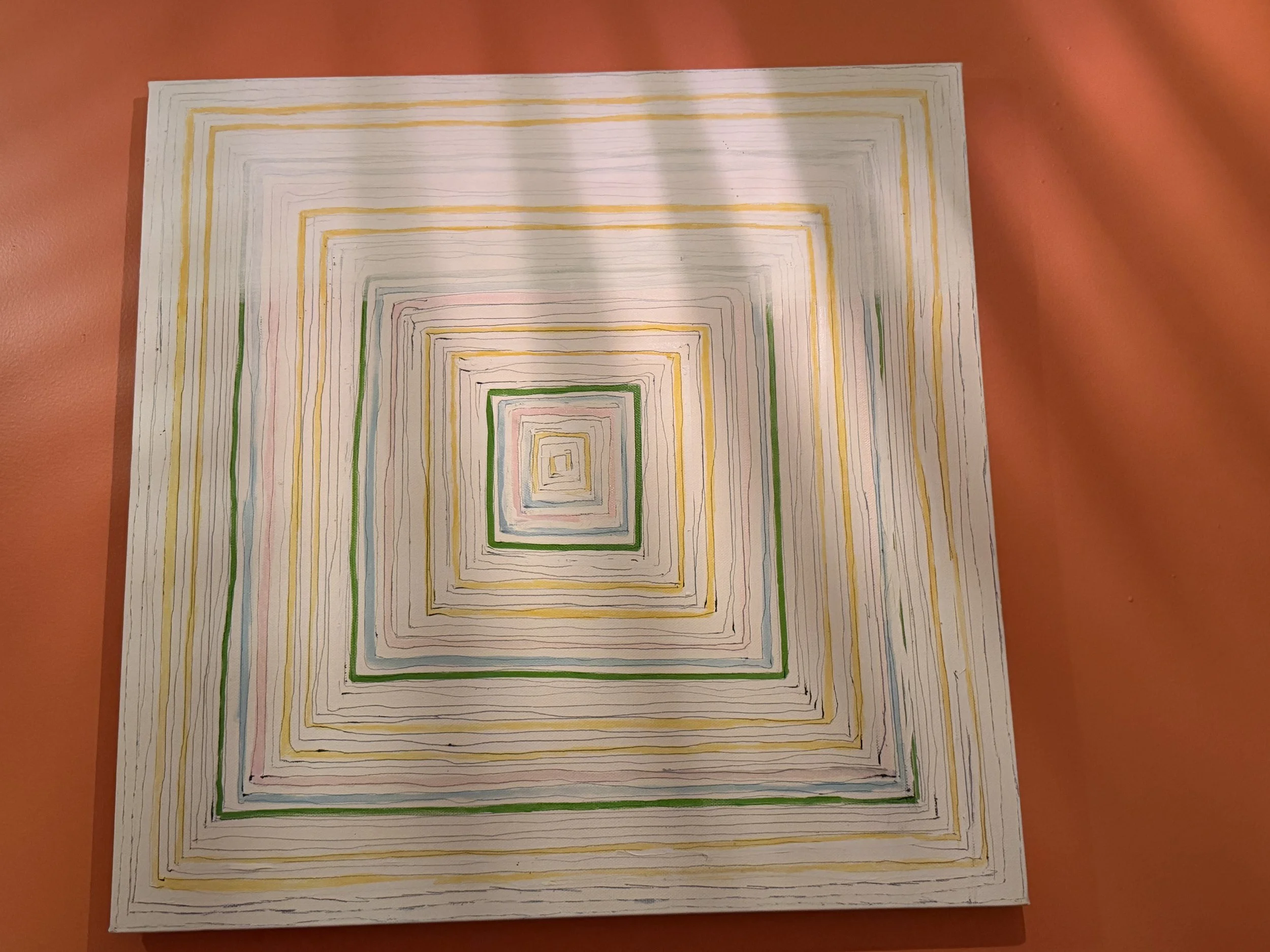 A piece of paper with multicolored concentric squares drawn on it, placed on a pink surface.