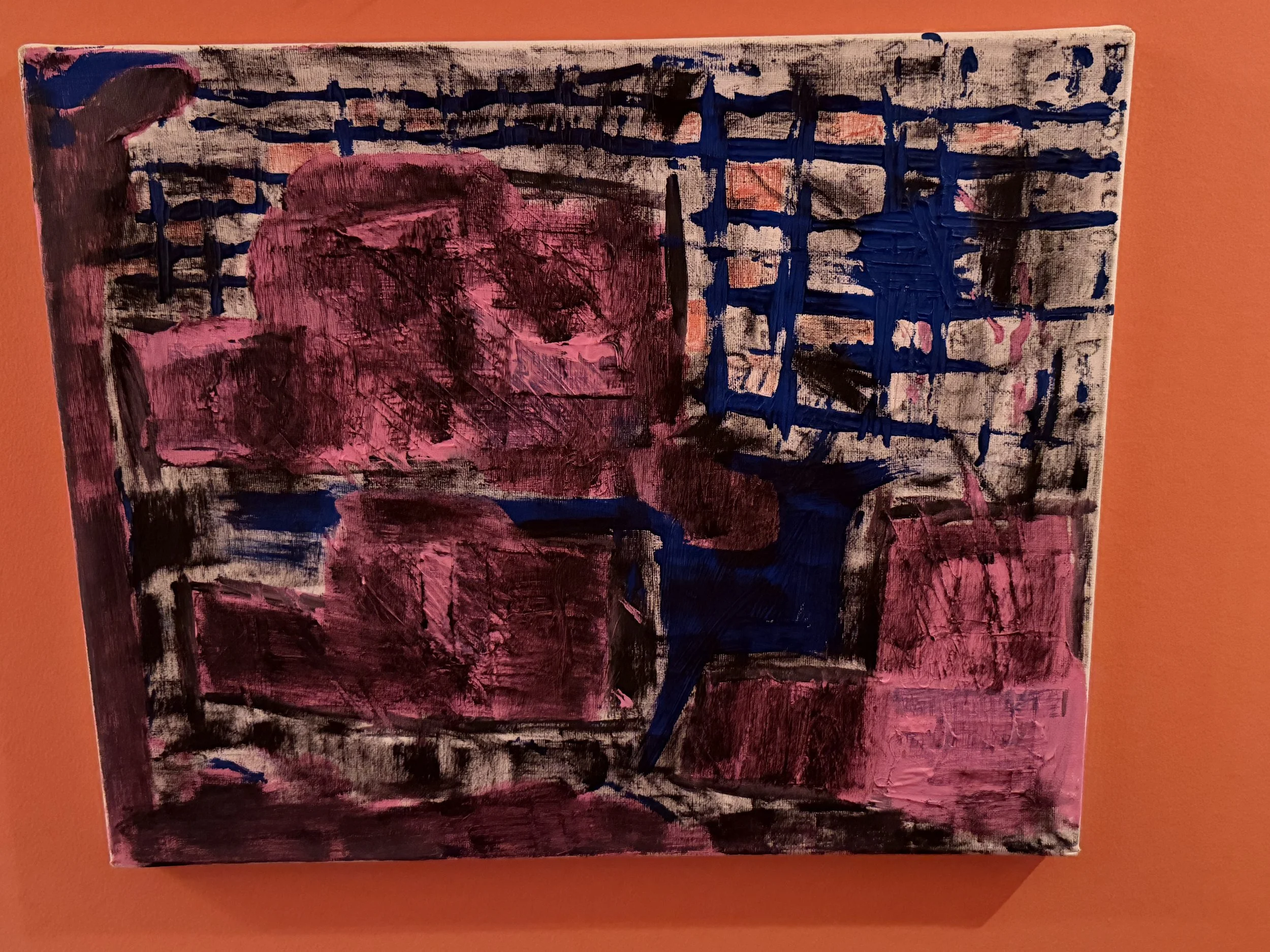 Abstract painting on canvas with black, pink, and blue brushstrokes, displayed on an orange wall.