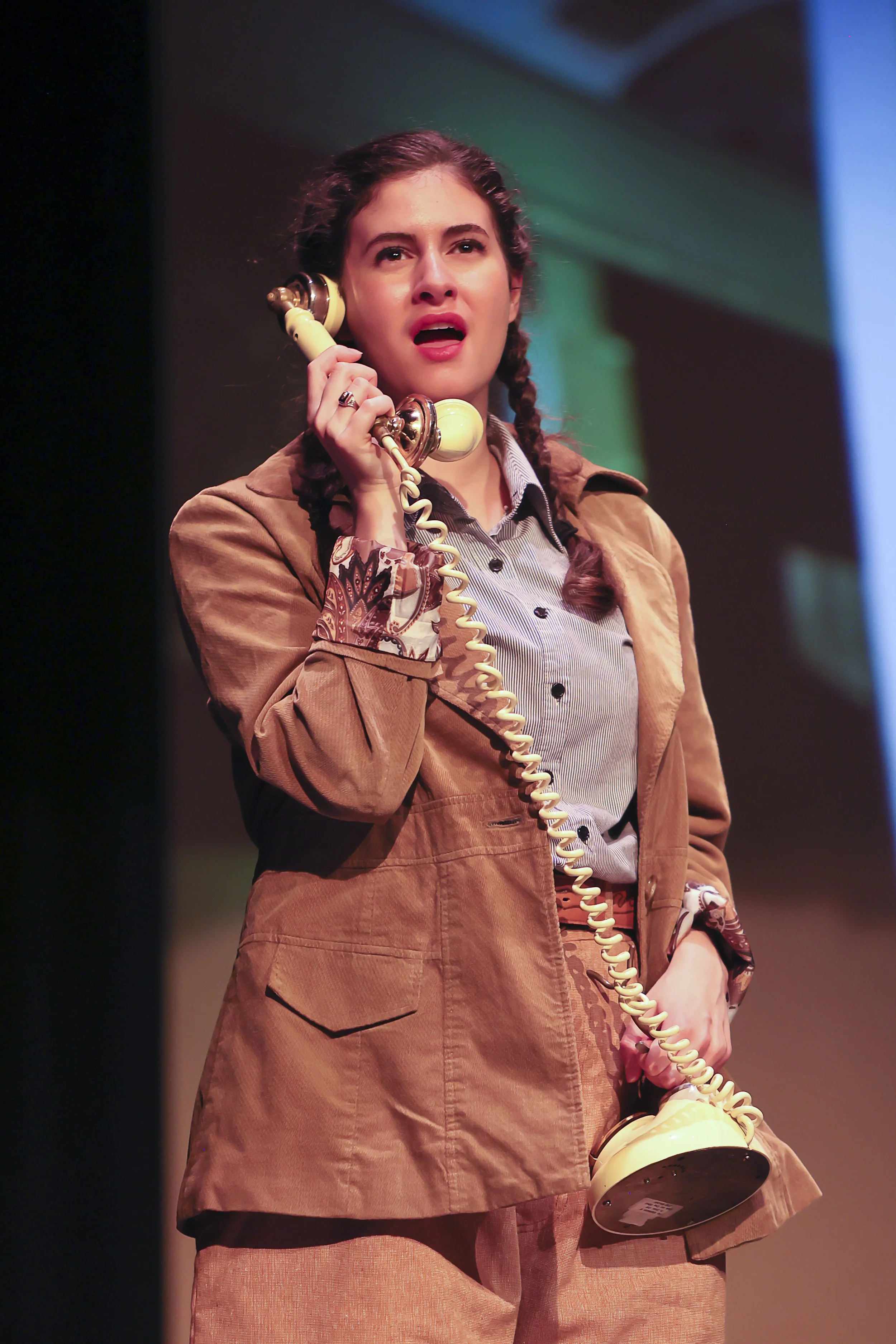 Isabella speaking into dial phone on stage in Staggerwing