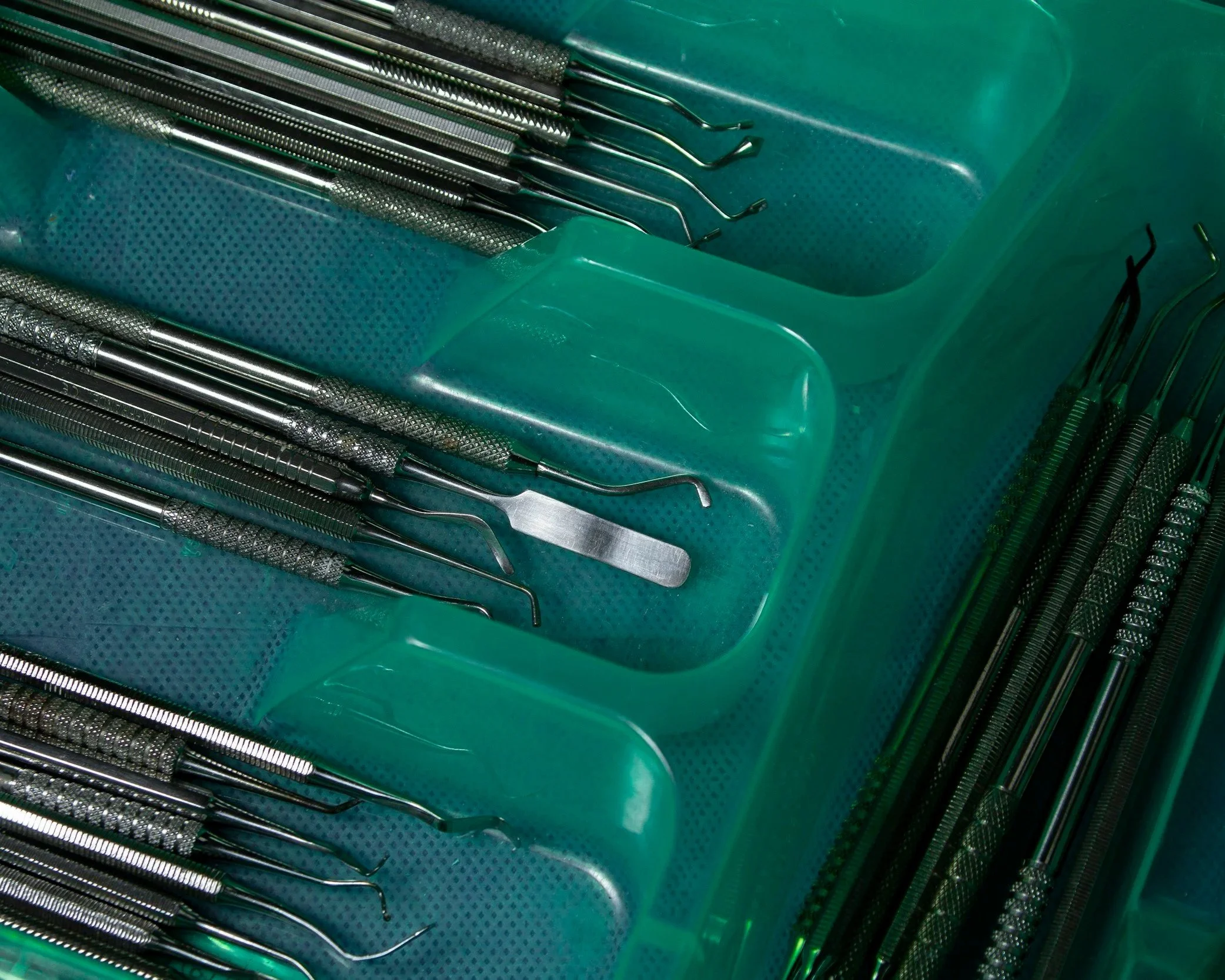 A tray of dental dental tools including probes, explorers, scalers, and a mirror, arranged in green plastic compartments.