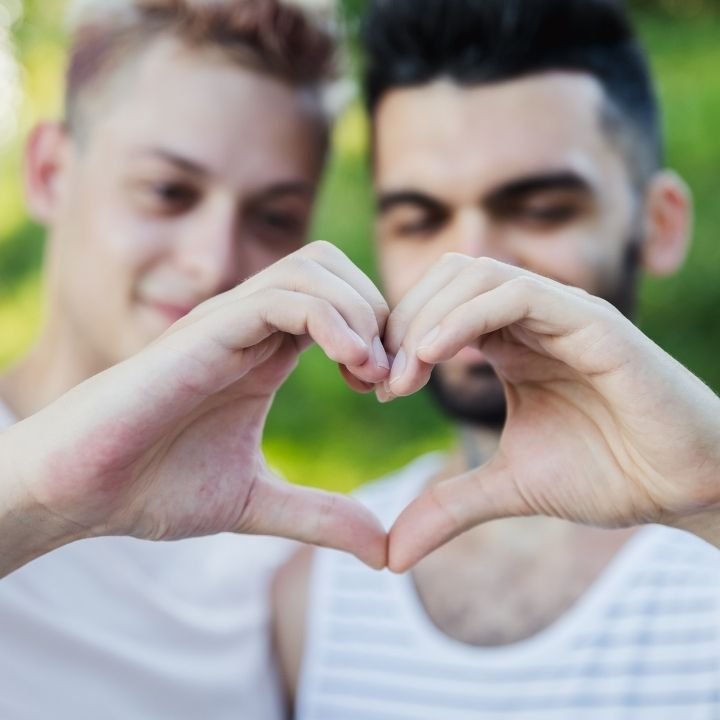 Two men outside making a heart shape with their hands.