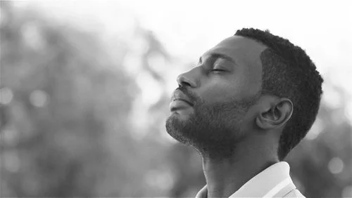 A man with closed eyes and a peaceful expression, outdoors, in black and white.