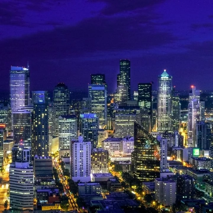 Nighttime aerial view of a city skyline with illuminated skyscrapers and tall buildings under a dark sky.