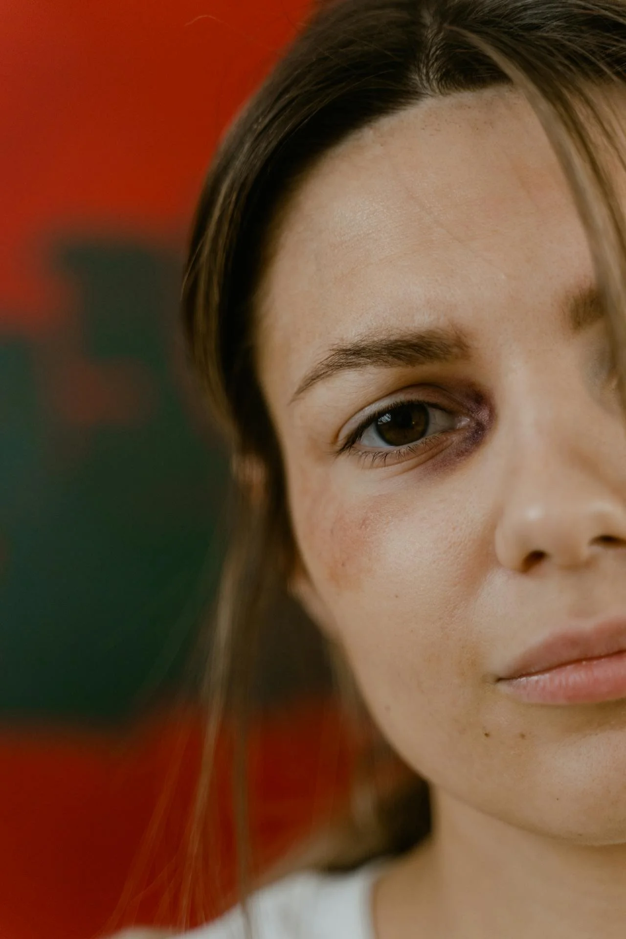 Close-up of a woman's face showing her right eye and part of her mouth, with a blurred background featuring red and green colors.