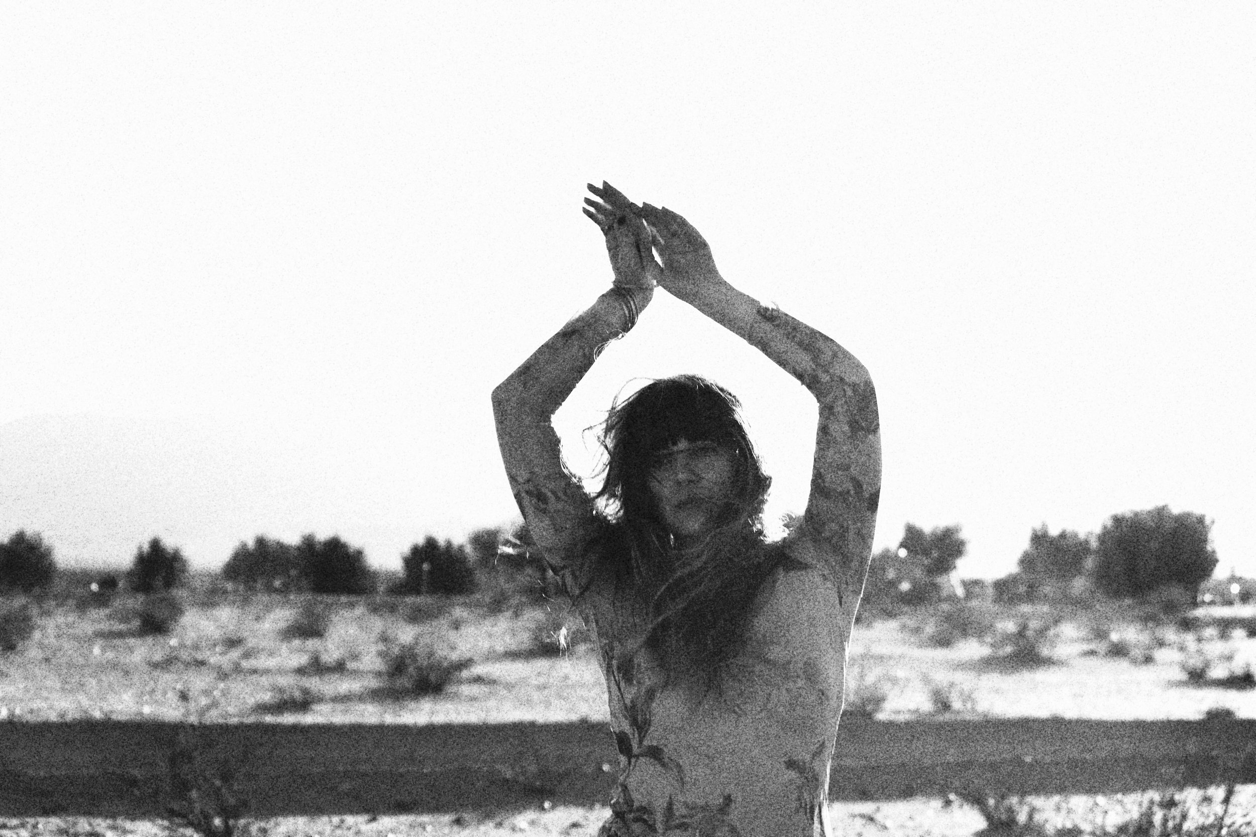 Black and white picture of a woman with her arms overhead and a desert with cactus in the background