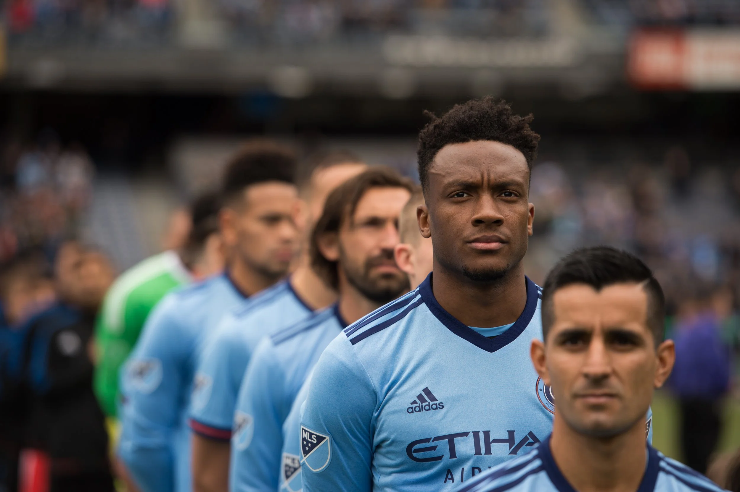 Soccer team players in blue jerseys standing in a line on a field with a blurred background.