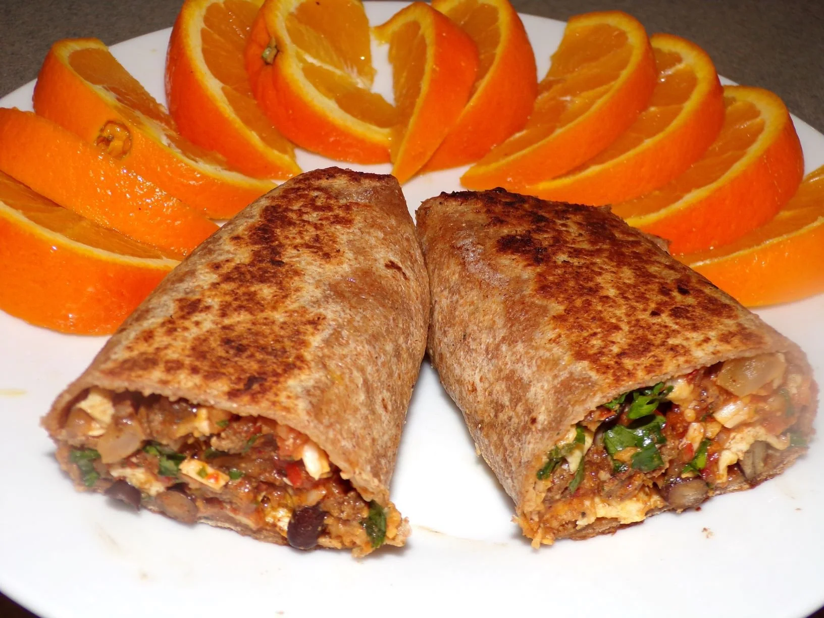 Breakfast Burrito sliced in half and arranged on a plate with orange slices