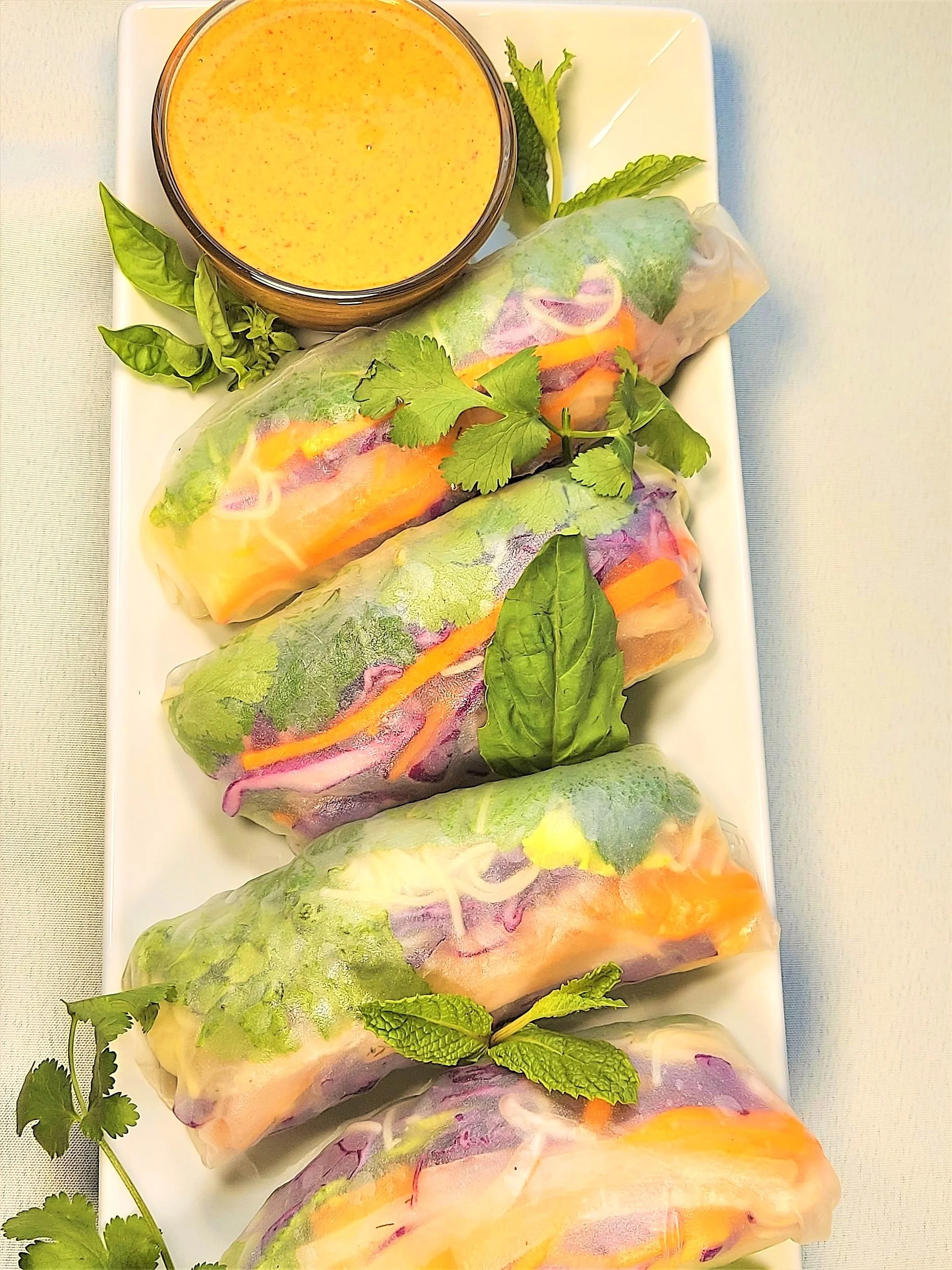 Tofu Spring Rolls on a serving platter garnished with fresh herbs and almond butter sauce