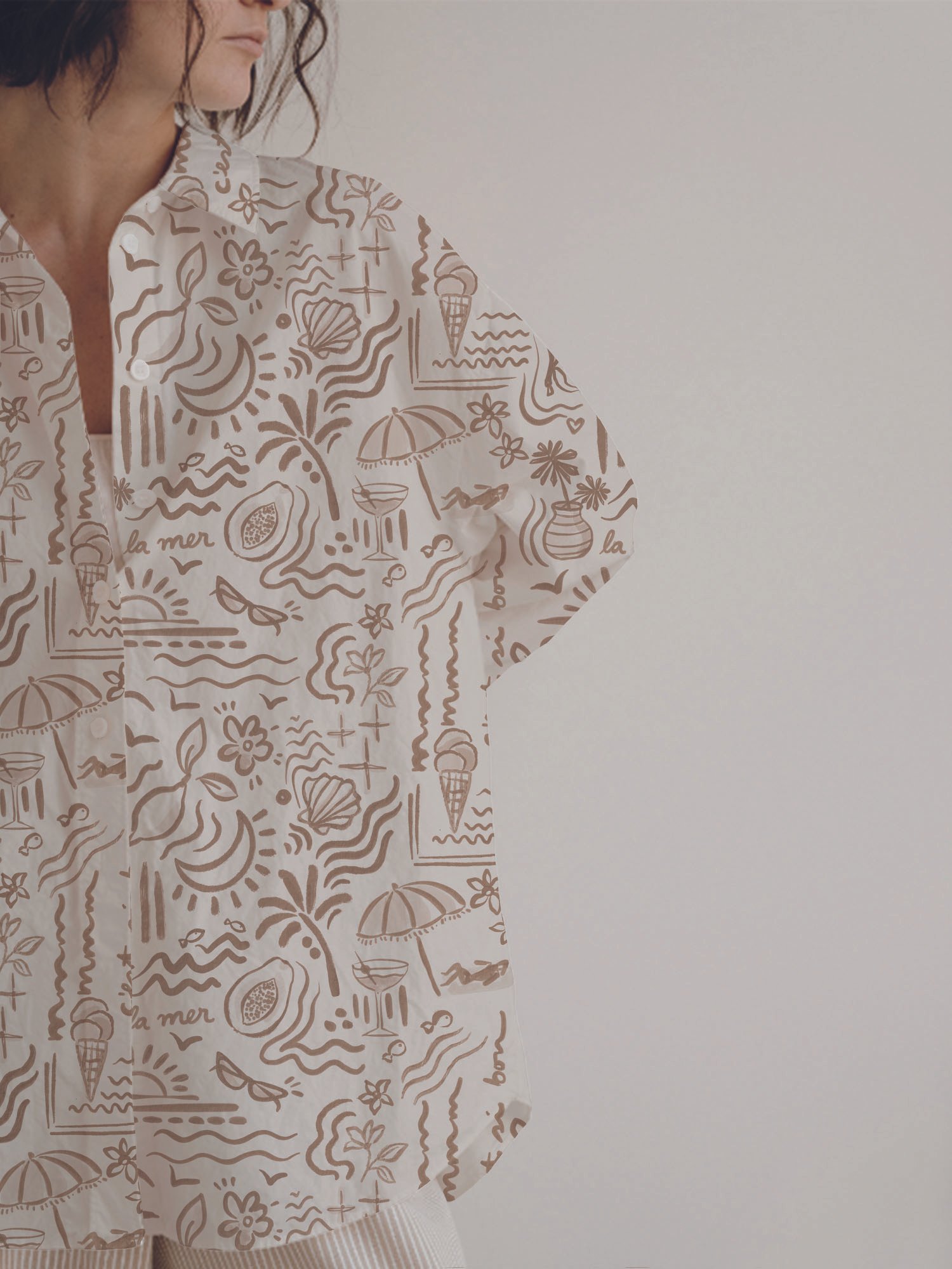 A person is wearing a button-up shirt with summer-themed illustrations including palm trees, sailboats, ice cream cones, umbrellas, and the words "la mer" and "bonheur" in a light brown color on a light background.