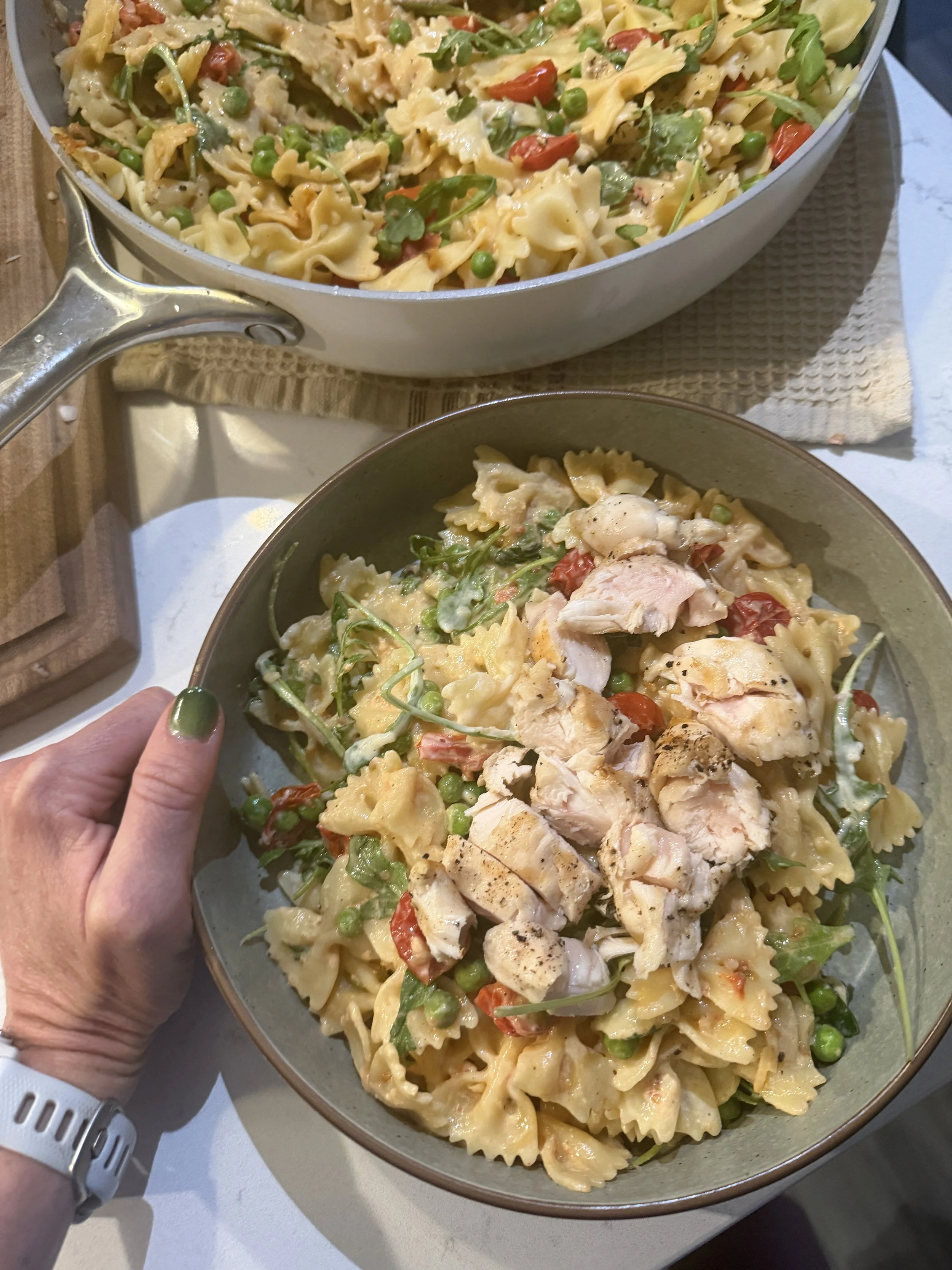 image of pasta with chicken and greek yogurt sauce in a bowl with a skillet of pasta in the background