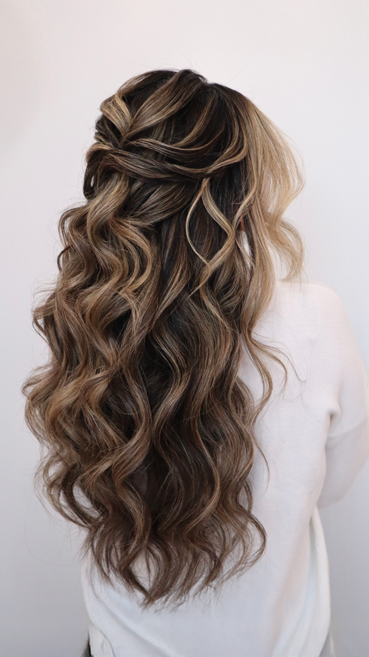 Side view of a woman with long, wavy, brown hair styled with blonde highlights, wearing a white top.