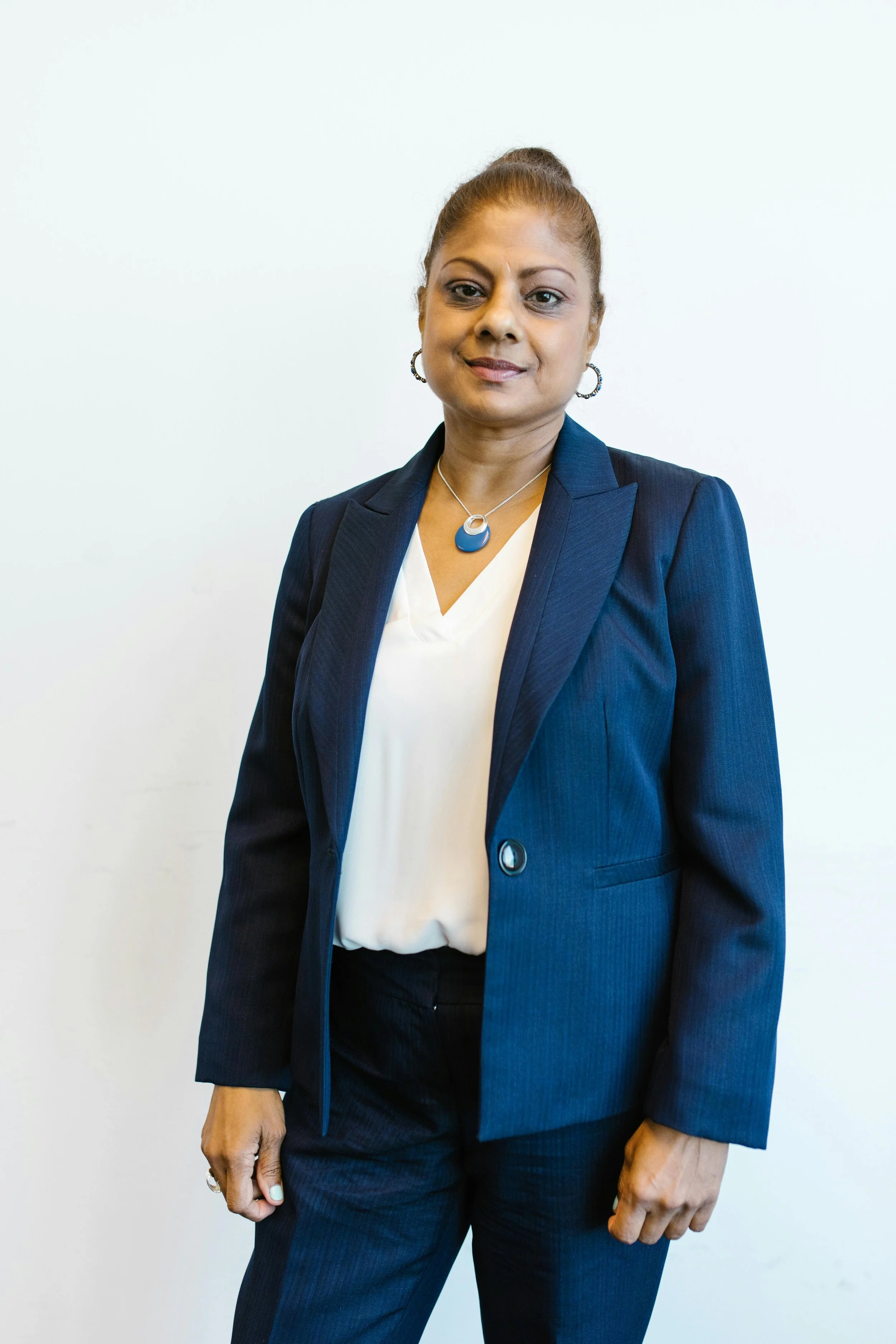 A professional woman in a dark blue blazer over a white blouse, standing against a plain white wall.