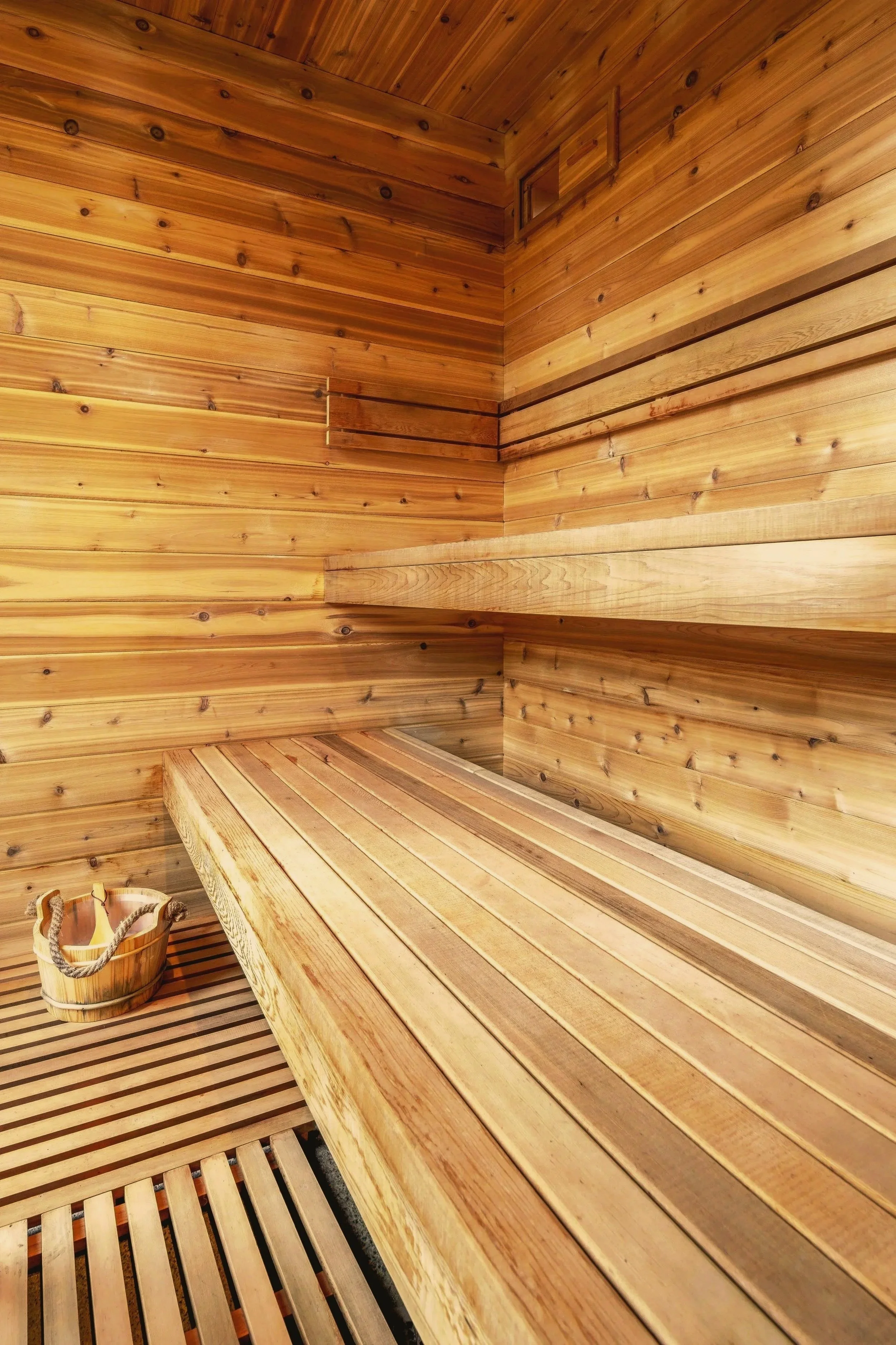 Interior view of a wooden sauna room with wooden benches and a bucket with a ladle.
