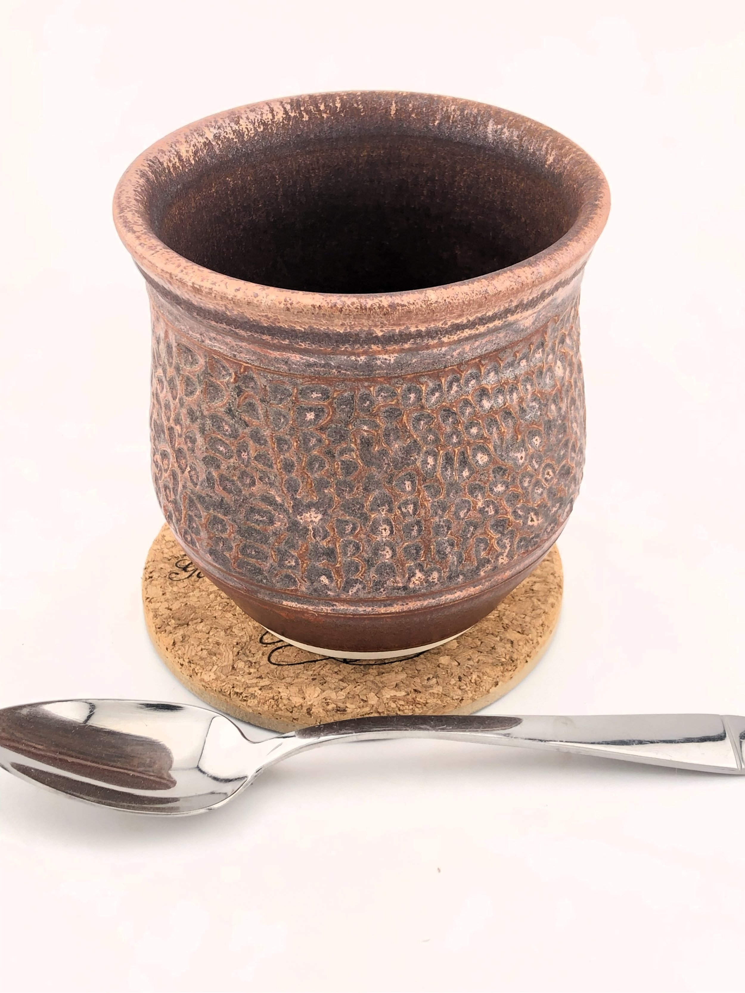 Textured ceramic mug on a cork coaster with a stainless steel spoon beside it.