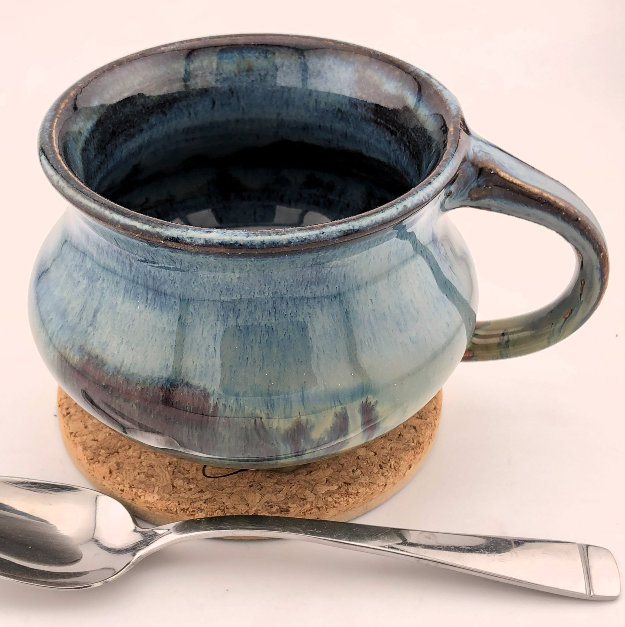 Blue ceramic mug on cork coaster with spoon beside it