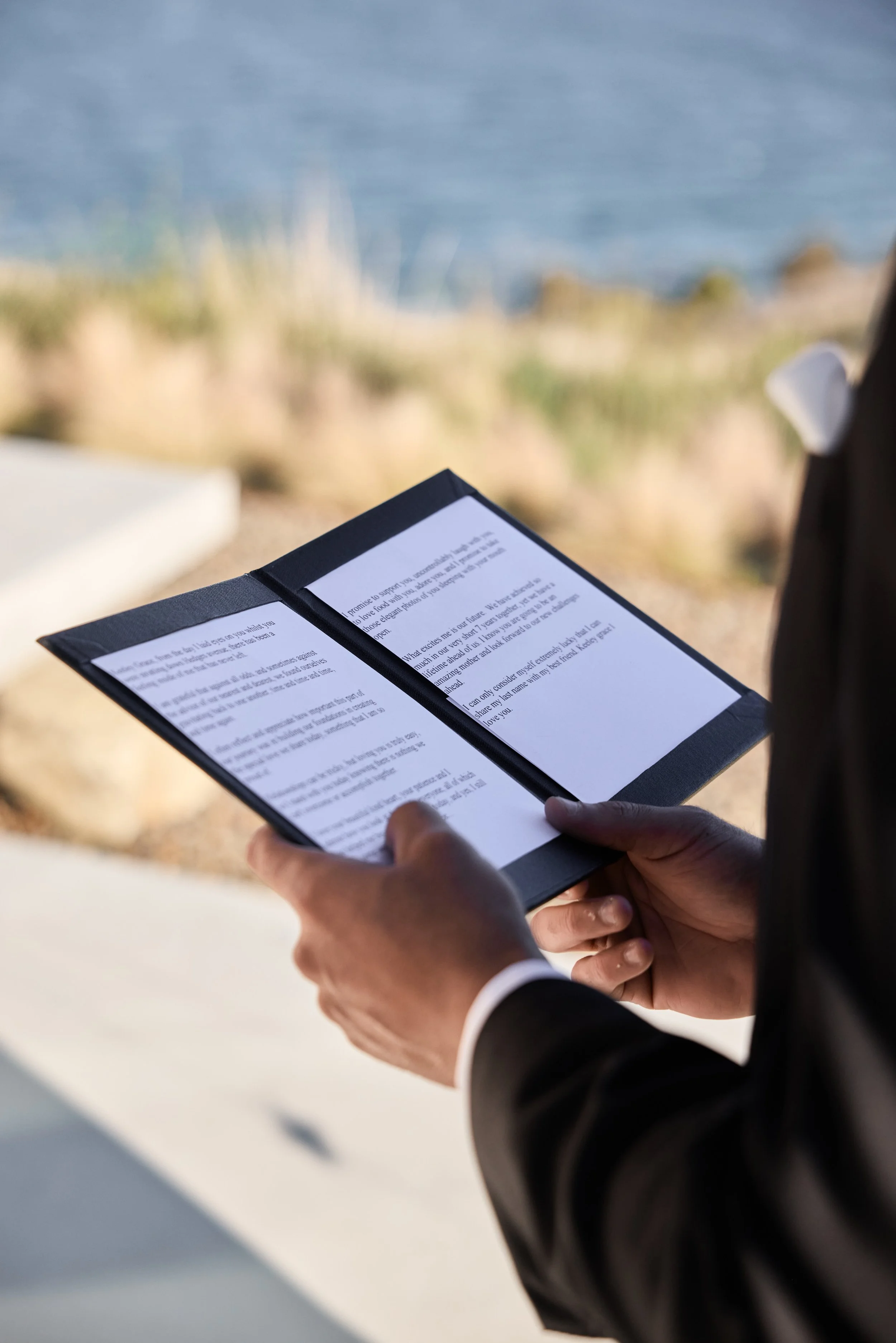 Person in a suit holding a book or menu outdoors near water