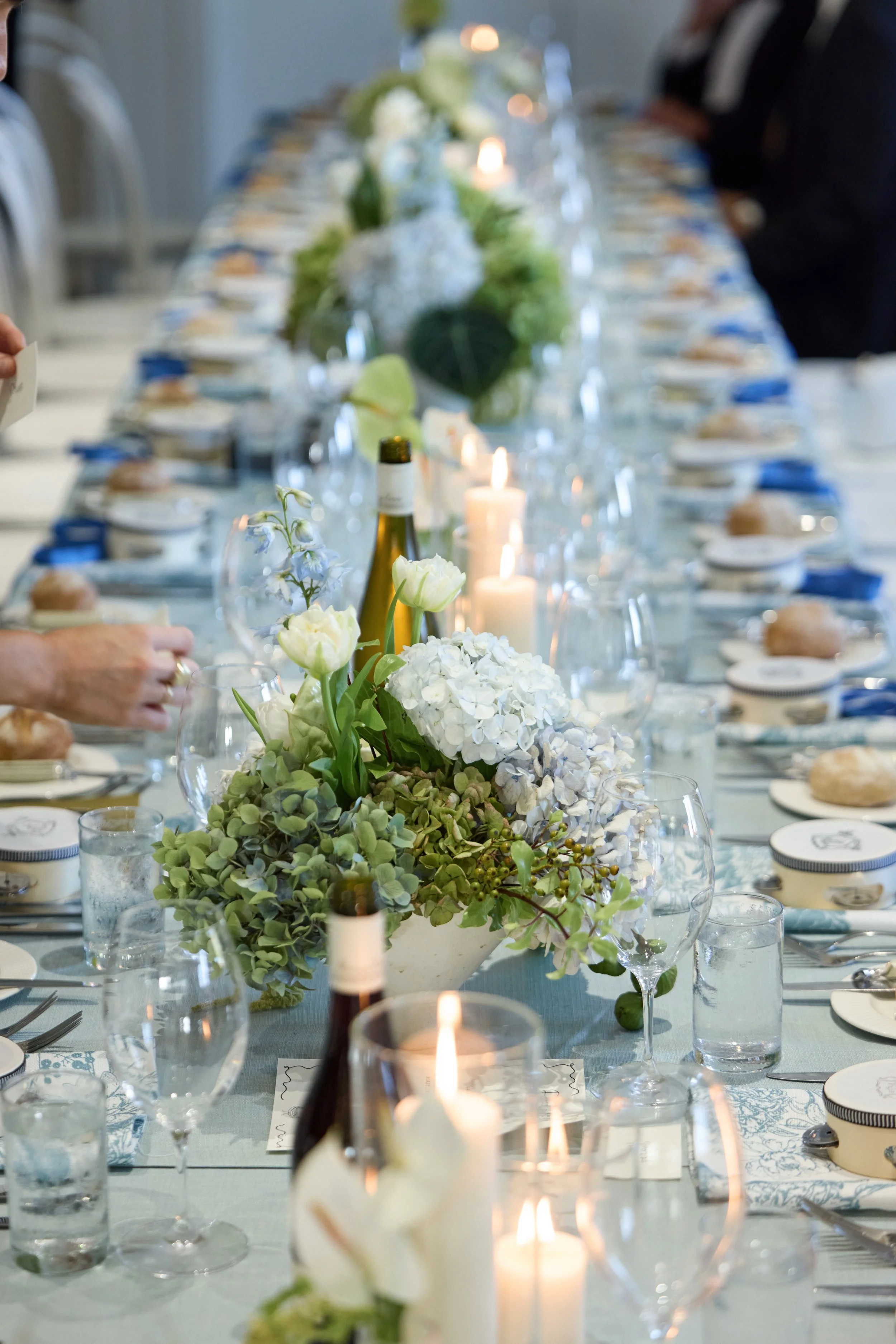 Elegant dining table decorated with white and green floral centerpieces, candles, and glassware, set for a formal event.