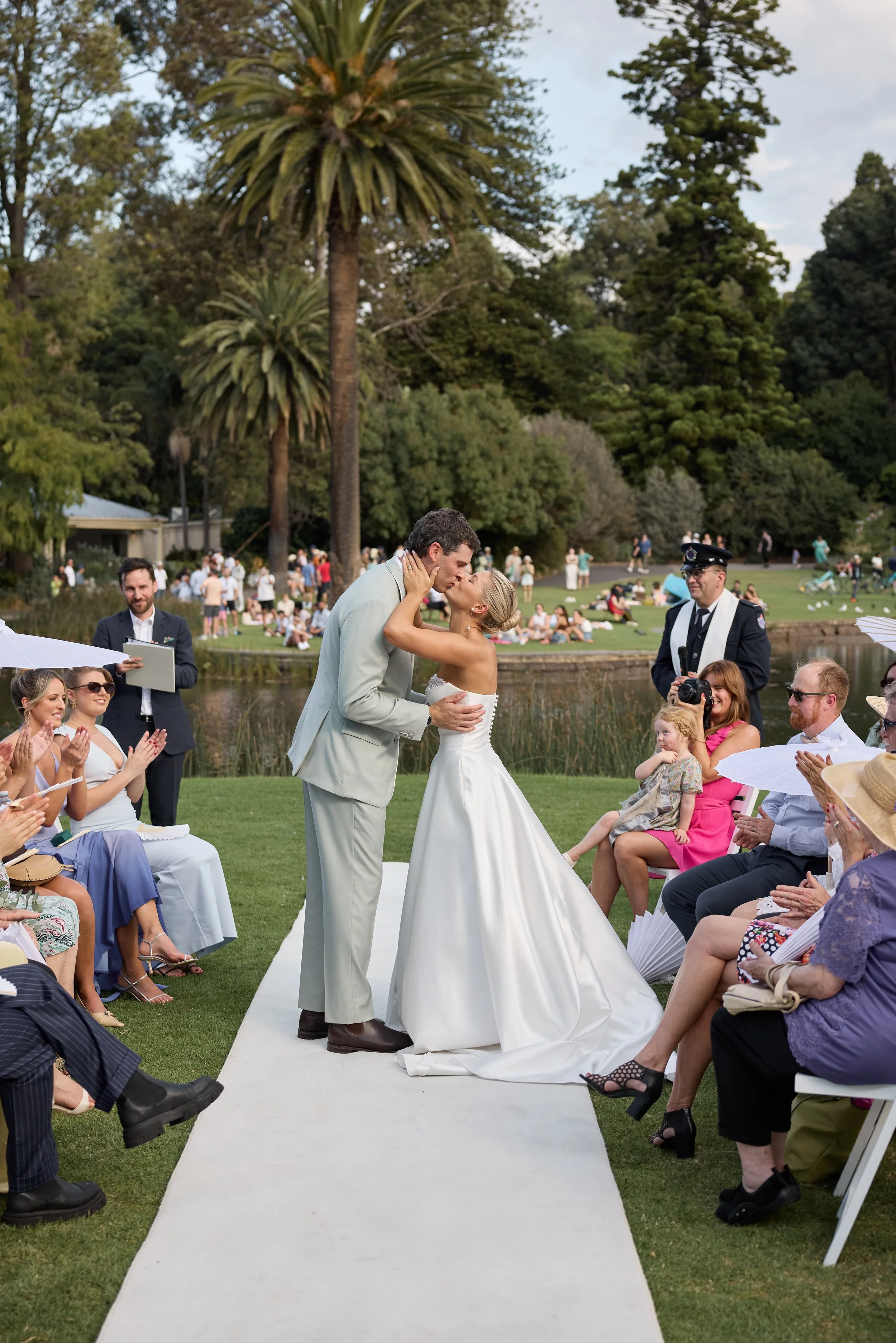 Bride and groom kissing during outdoor wedding ceremony with guests clapping and smiling.