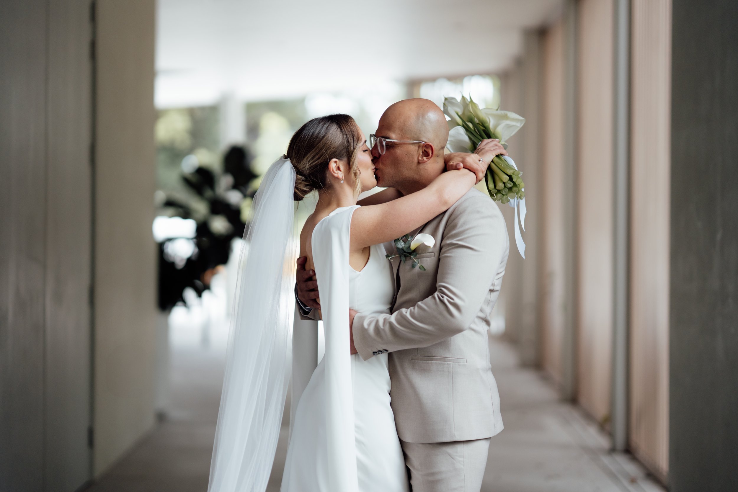 A bride and groom kissing, bride holding a bouquet, indoor setting.