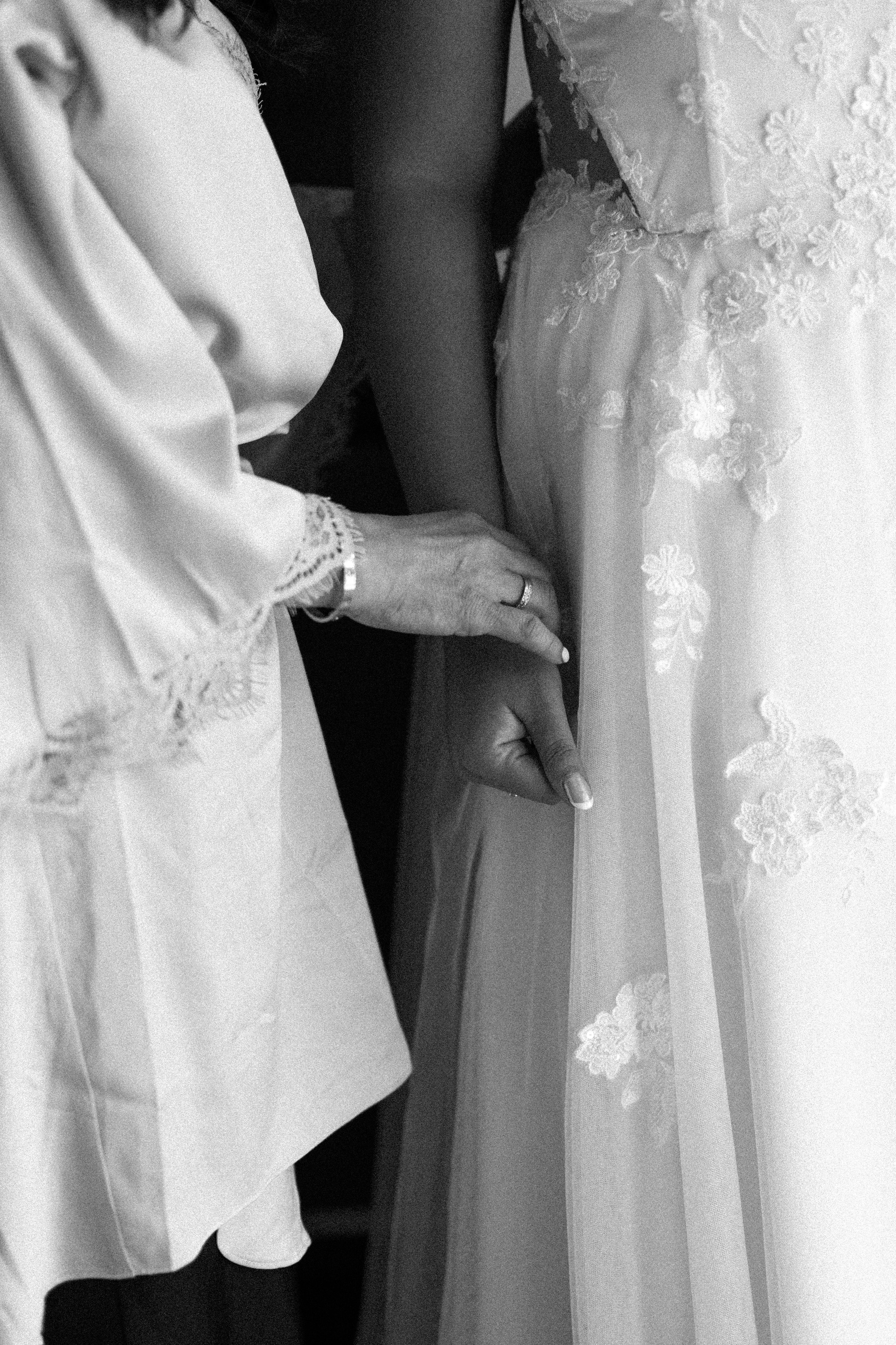 Bride in a lace wedding dress with a hand holding the gown's fabric.