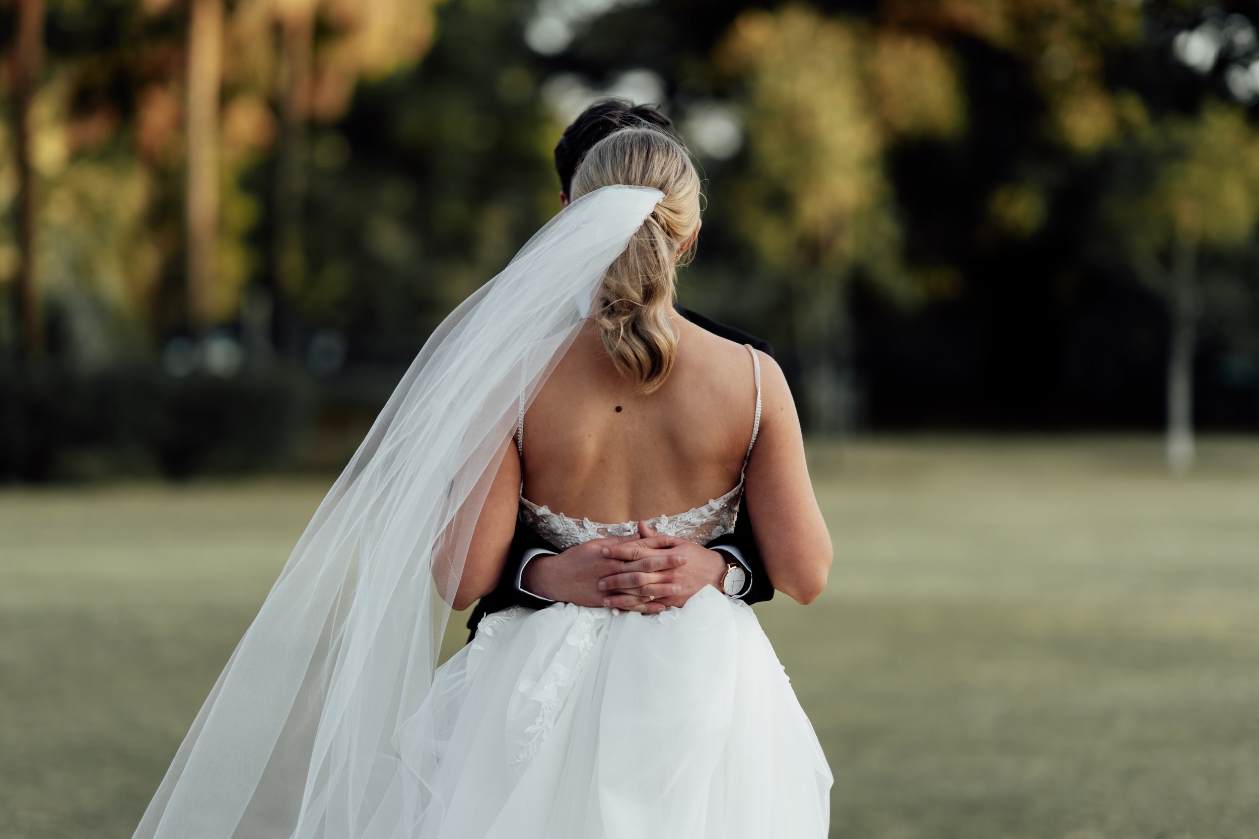 Bride and groom embracing outdoors, bride wearing a long veil, groom in a suit.