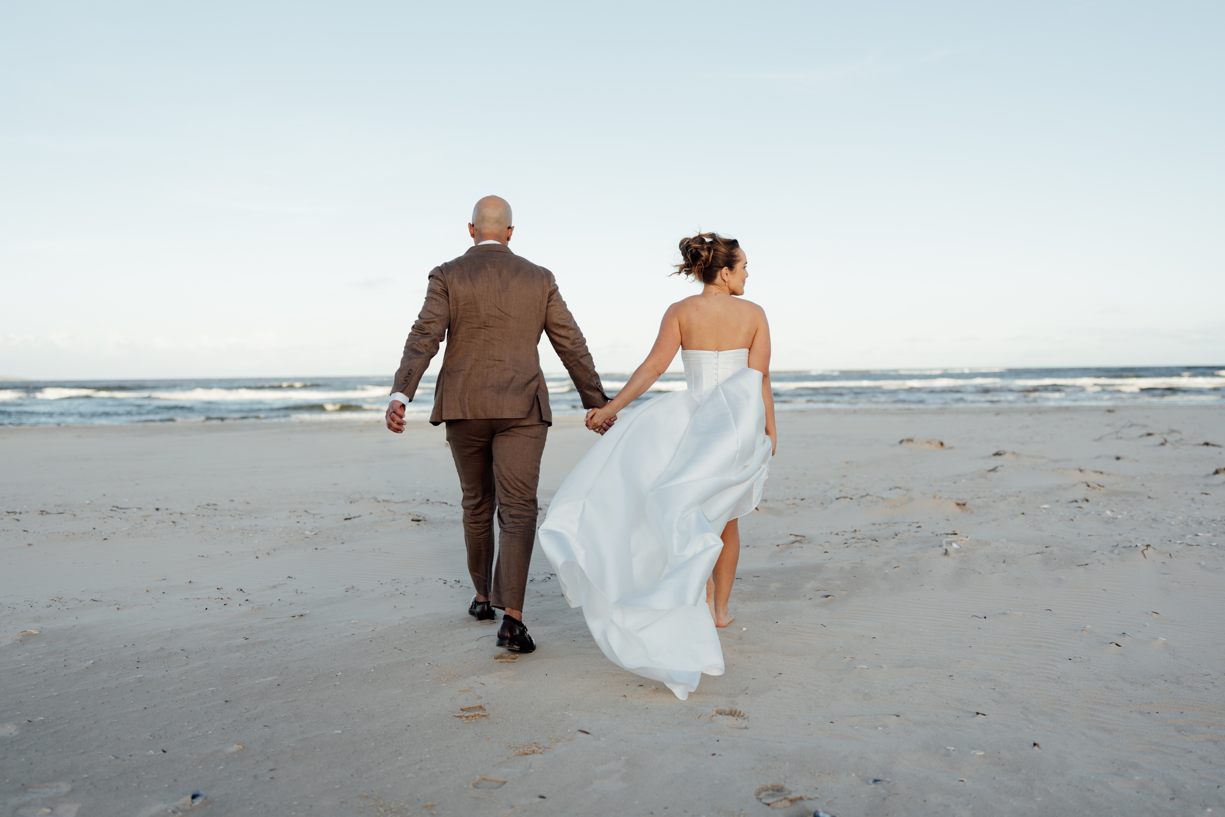 A newlywed couple sharing a kiss outside a building, with greenery and hanging lights in the background.