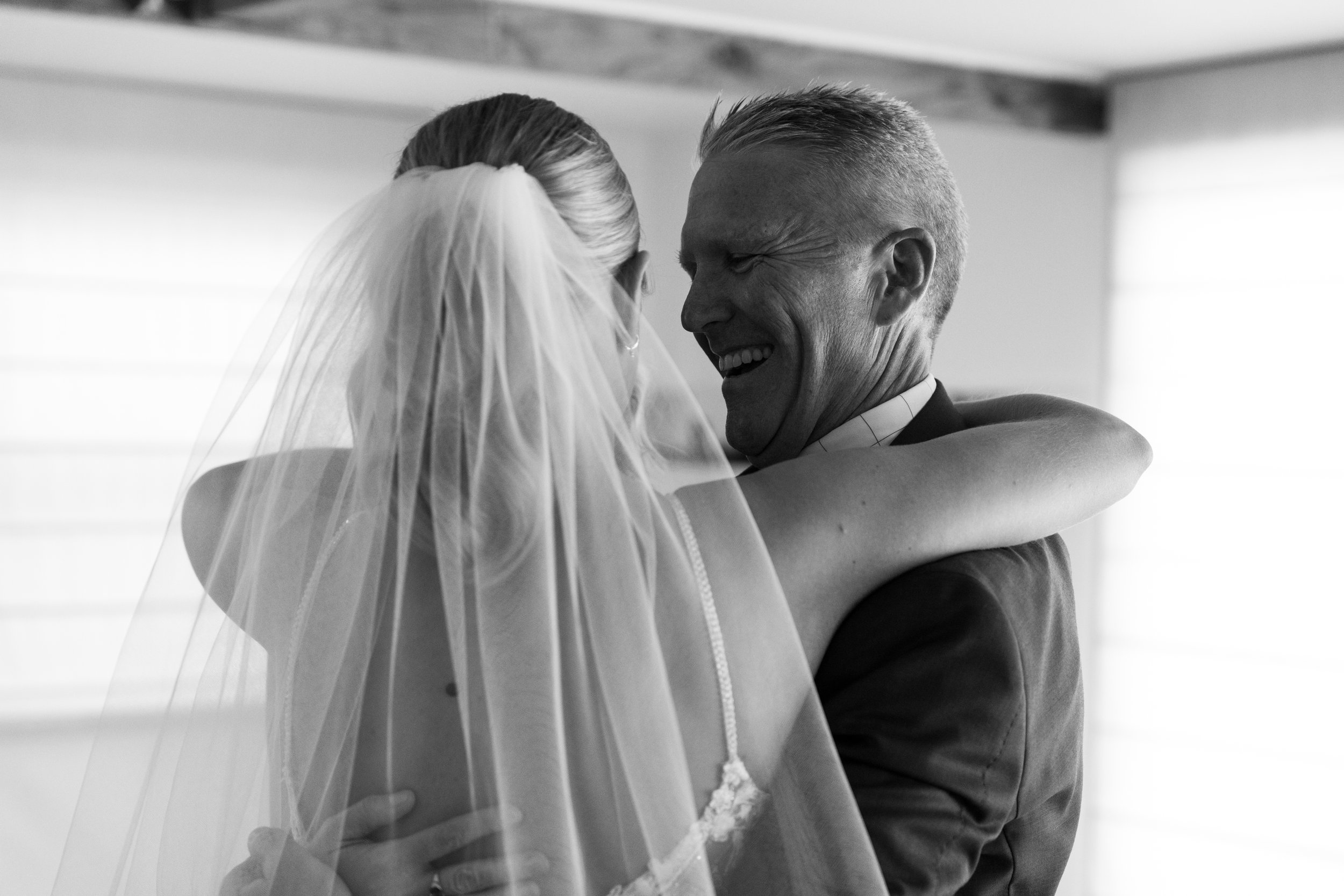 Black and white photo of a bride in a veil hugging a man in a suit.