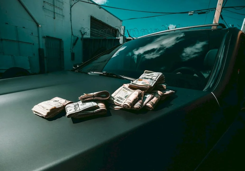 Bundles of cash on the hood of a black pickup truck parked outdoors.