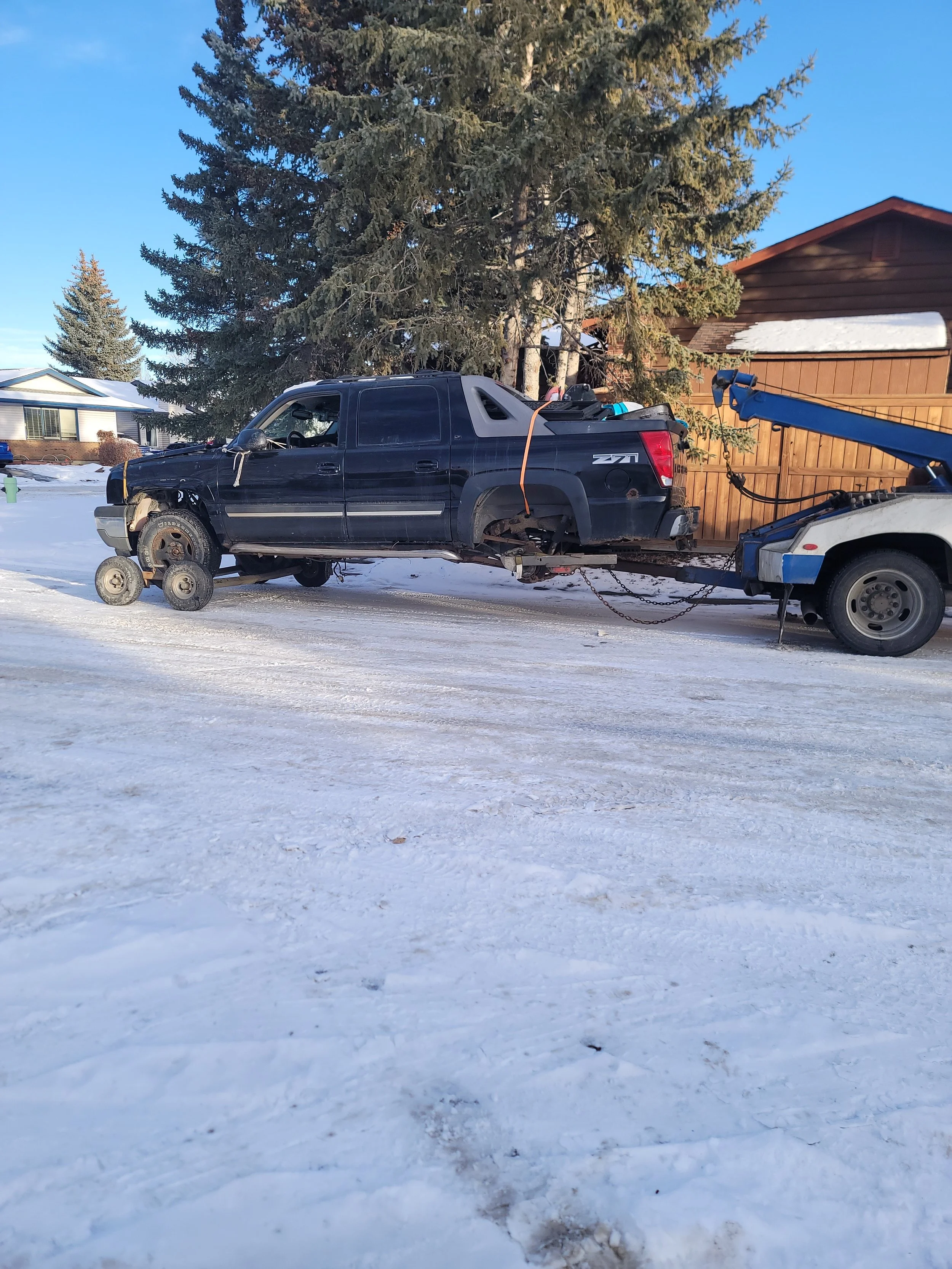 A black pickup truck with no wheels being towed on a snowy road during daytime.