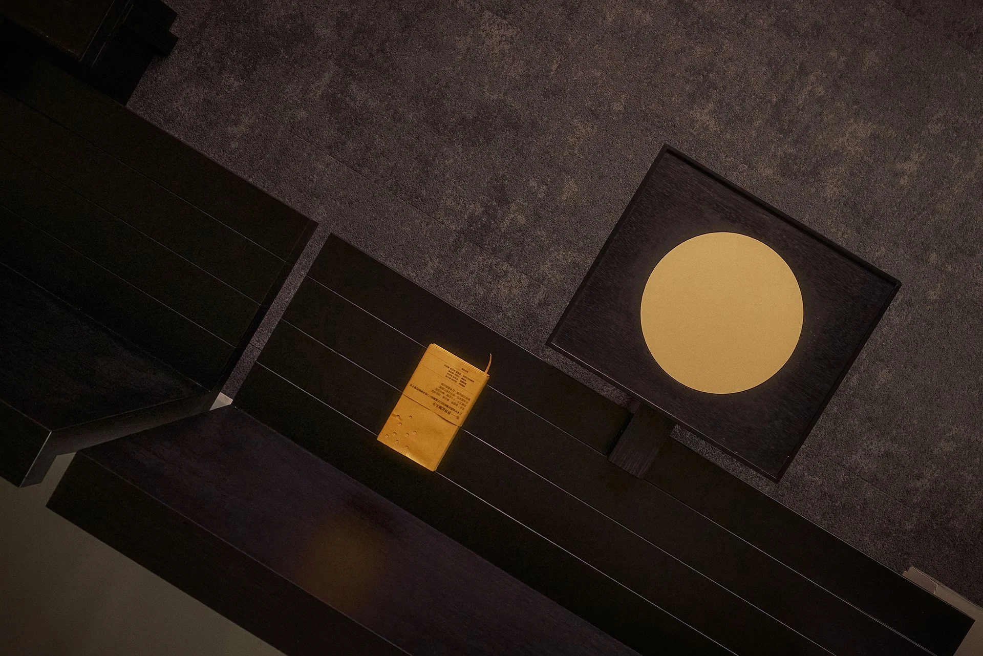 A dark, textured ceiling with a square light fixture and a bench with a yellow booklet resting on it.