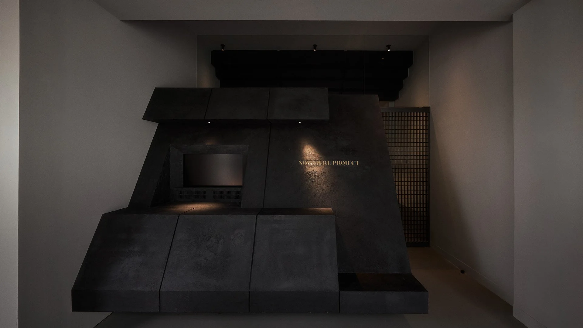 Dark, geometric installation with a small screen and illuminated text reading 'Venture Project' in a minimalist, modern space.