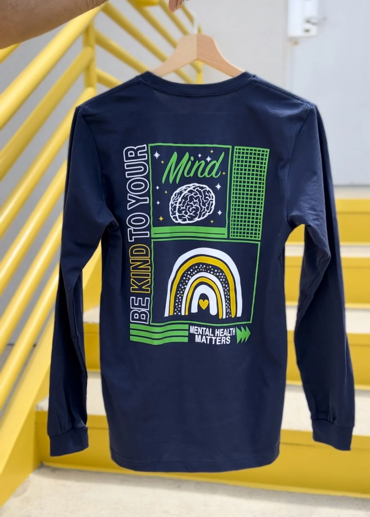 Navy long-sleeve shirt with "Be Kind to Your Mind" and "Mental Health Matters" text, brain and rainbow graphics.