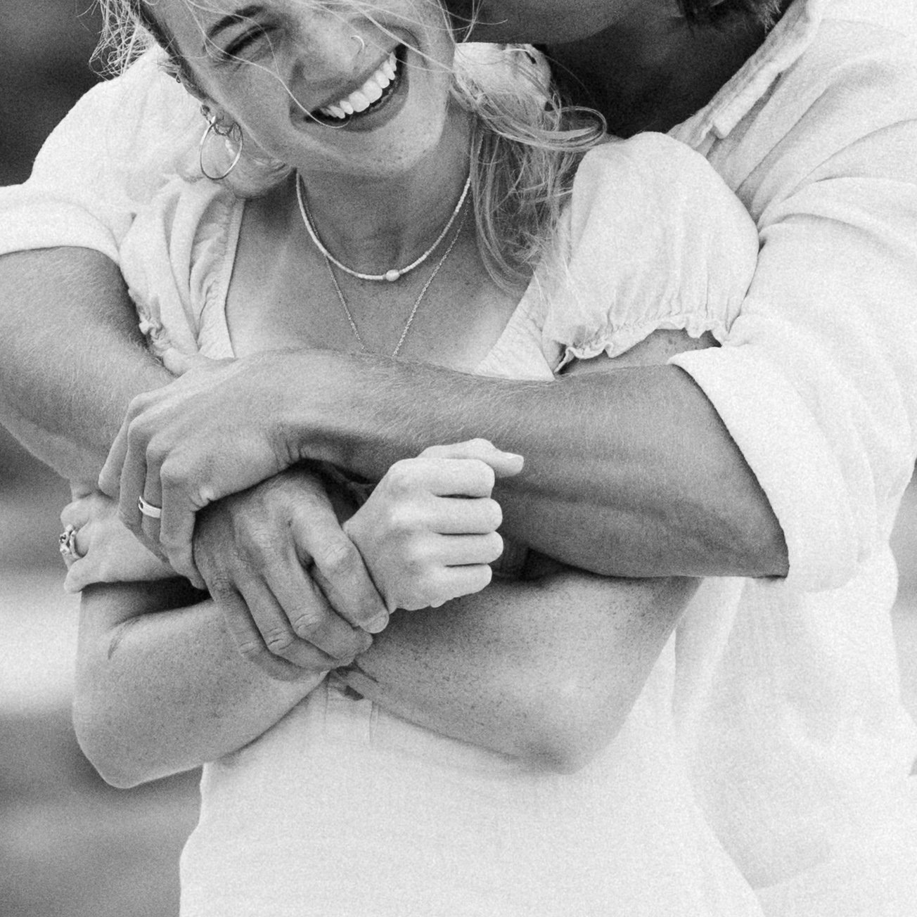 A couple smiling and wearing jewelry, embracing someone with an arm around her shoulder.