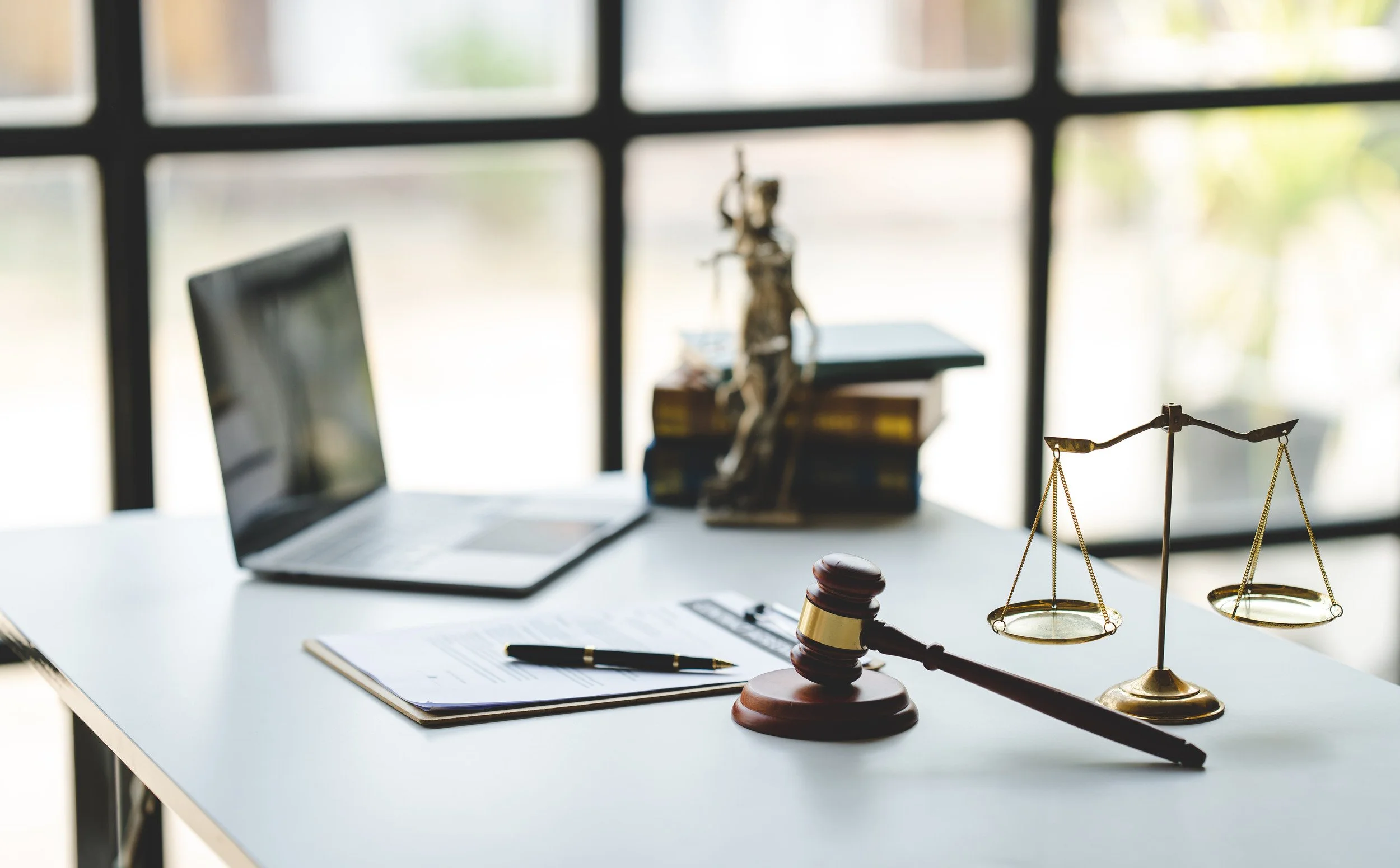 Legal office desk with a gavel, scales of justice, a laptop, and legal documents on a clipboard.