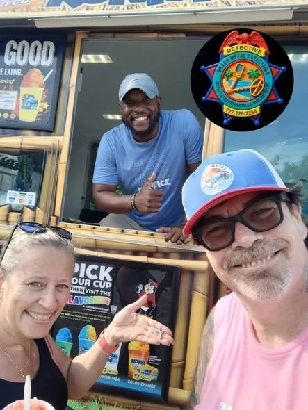 Smiling woman pointing at a cartoon character on an ice cream truck with a man taking a selfie in front of it, and another man leaning out of the truck window giving a thumbs up. The truck features a colorful logo with a detective badge and palm trees.