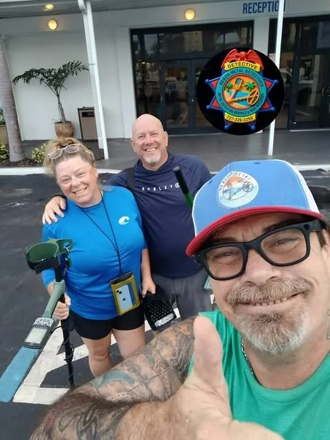 Three people smiling outside a building with a sign reading 'Reception' and a badge logo for a detective agency in the background. One man is taking a selfie, wearing a blue and red cap, glasses, and a green shirt, giving a thumbs-up. A woman and another man are standing behind him, dressed casually and smiling.