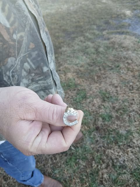 Person holding a silver ring with a large stone in an outdoor grassy area.