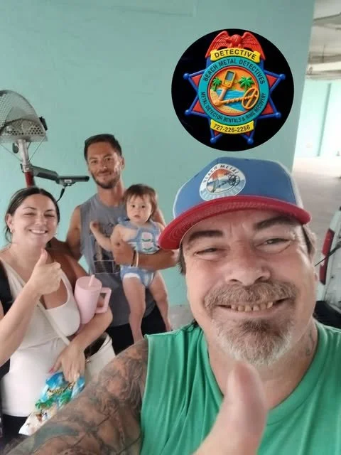 A smiling group of four people, including a man wearing a baseball cap, a woman, a man holding a small child, all in a hallway, with a logo for a metal detector service in the top right corner.