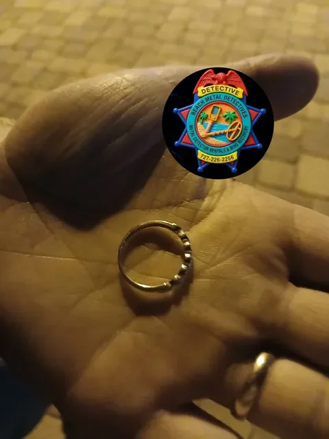 A person's hand holding a small ring with a Detective badge sticker nearby.
