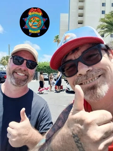 Two smiling men wearing sunglasses and baseball caps, giving thumbs-up gestures outdoors in a parking lot with palm trees. A logo with a sheriff badge and the words "Detective" and "Metal Detector" is superimposed on the top left corner of the image.