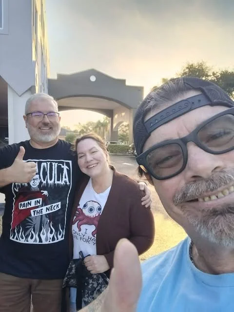 Three friends taking a selfie outdoors at sunset, smiling, with a building in the background.