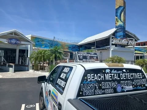 Beach metal detector business vehicle parked outside amusement park or water park with a roller coaster in the background.