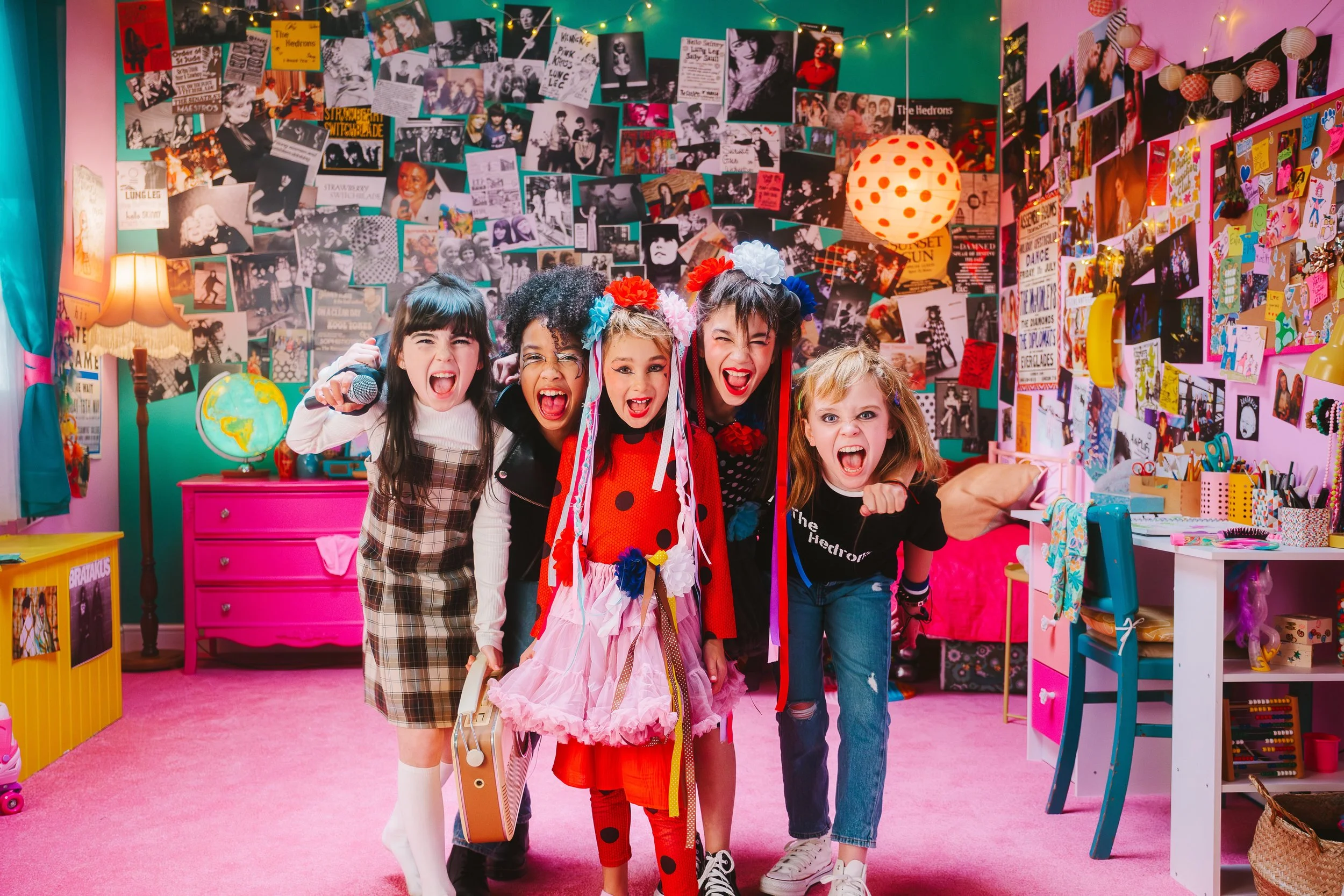 Still from Since Yesterday: The Untold Story Of Scotland's Girl Bands showing a group of fabulously punk young girls posing for a picture in a room plastered with punk imagery and with a pink floor