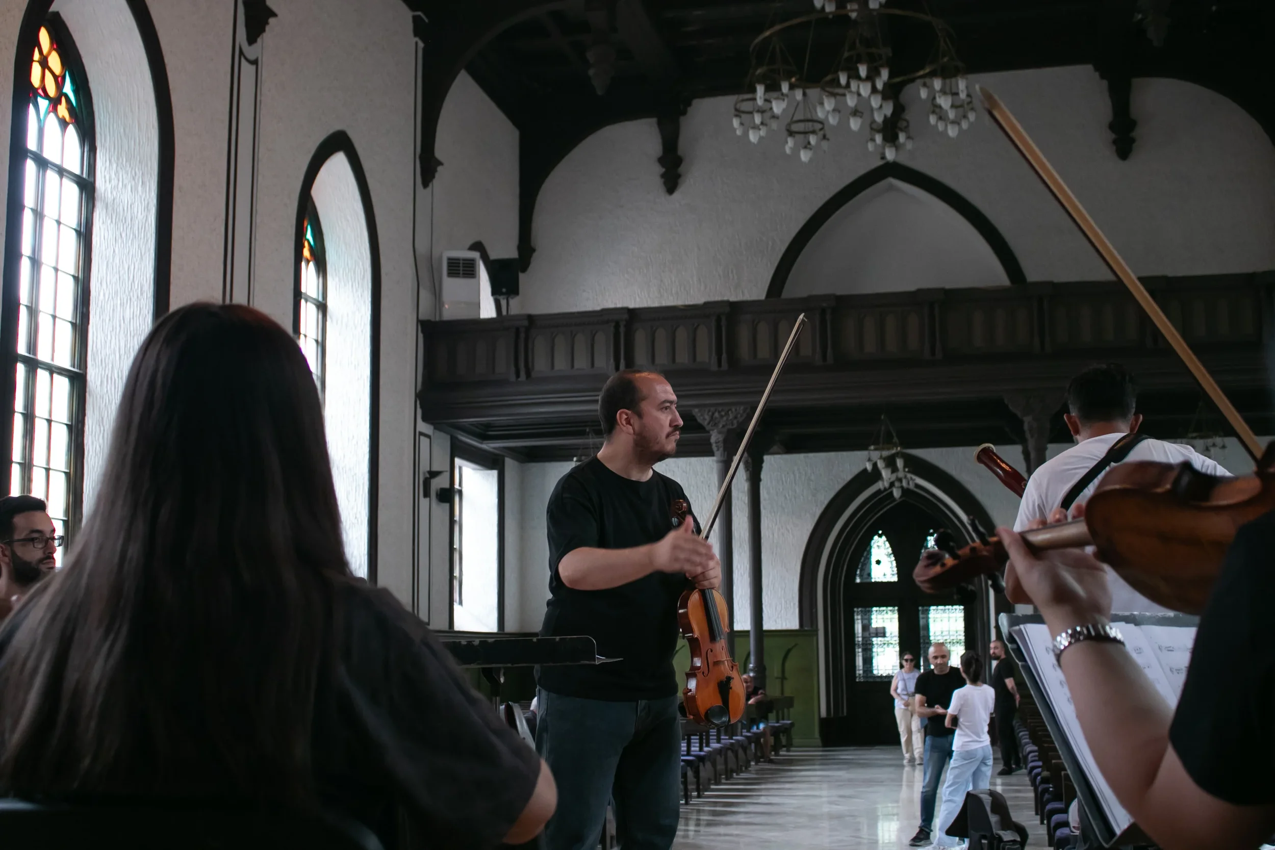 A group of musicians rehearsing inside a church with tall stained glass windows and wooden pews.
