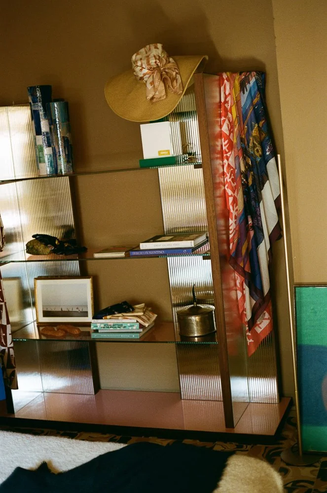 Scaffale con libri, una fotografia incorniciata, e vari oggetti decorativi, con un cappello a tesa larga e una sciarpa appesa sopra.