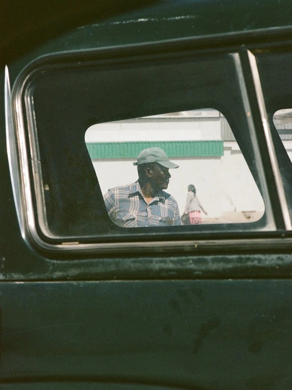 Un uomo con cappello e camicia a quadri visto attraverso un finestrino di un veicolo.