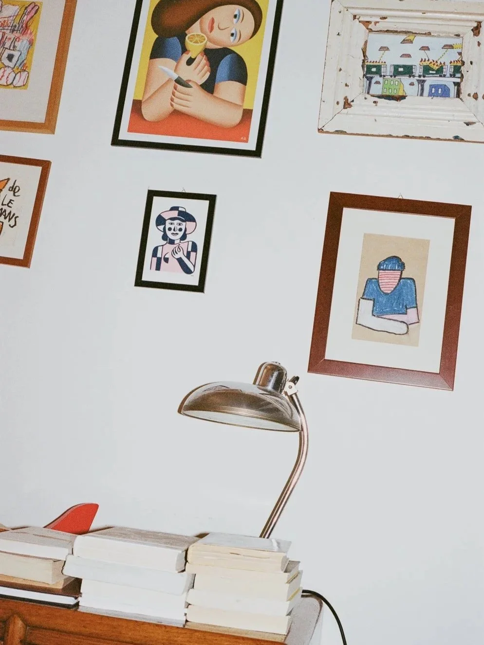 Pittura di una donna con cappello che tiene un limone e un coltello, quadro di una donna con cappello e braccia incrociate, quadro di un paesaggio con case colorate, e quadro di una persona con maglietta blu e testa coperta da una maschera. Sul tavol