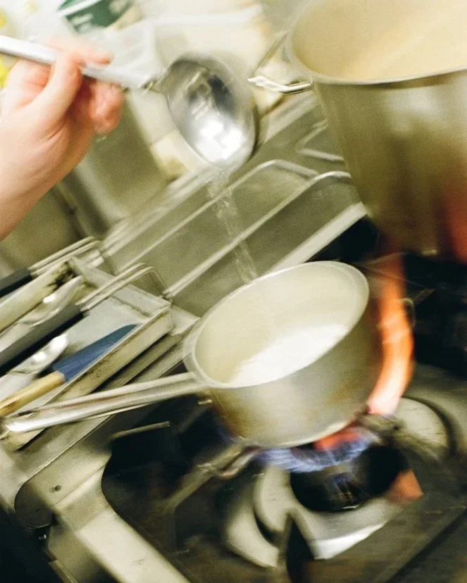Cucina professionale con pentola che bolle sul fornello a gas, acqua o ingrediente stuzzica sopra un pentolino, utensili da cucina sul bancone.
