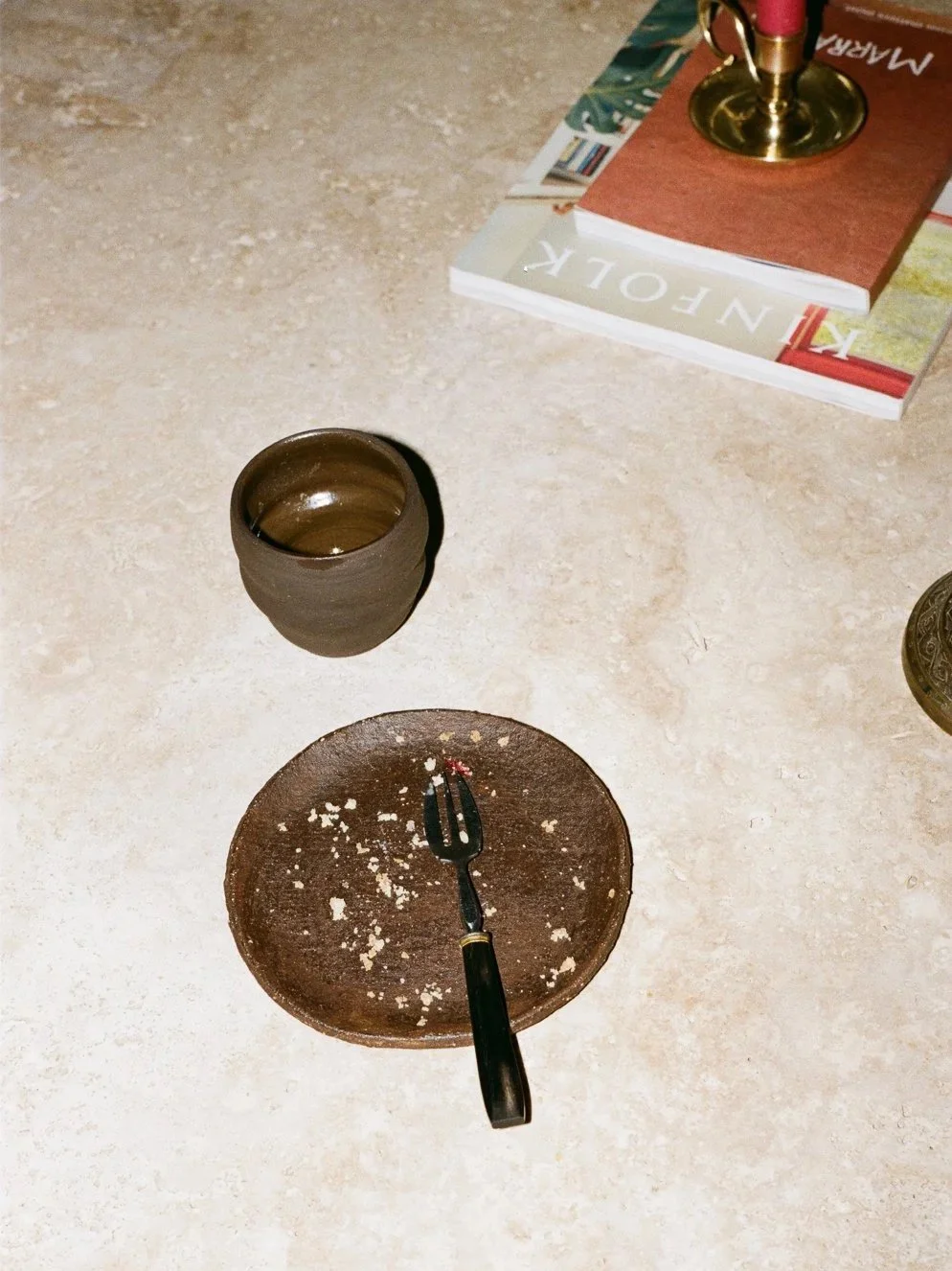 Piattino sporco con forchetta e briciole, bicchiere vuoto, libro e fumaiolo acceso, tutto su un tavolo.