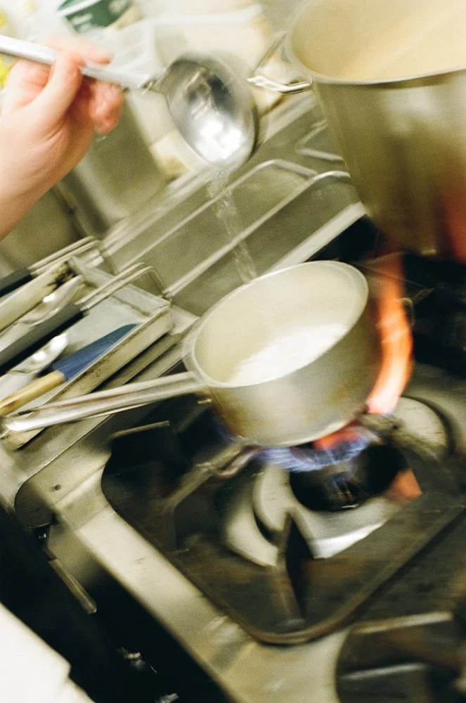 Cucina professionale con pentola che bolle sul fornello a gas, acqua o ingrediente stuzzica sopra un pentolino, utensili da cucina sul bancone.